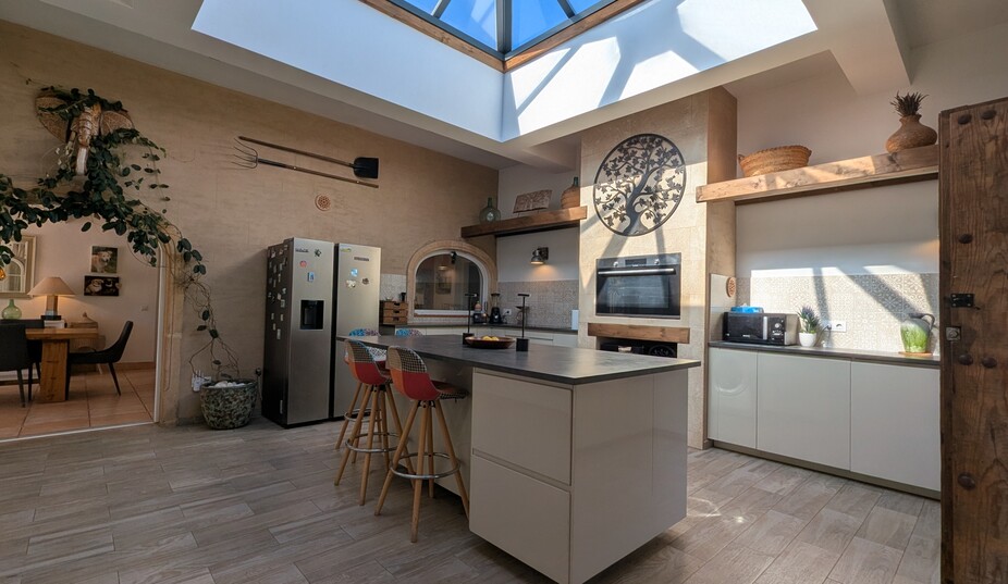 Moderne keuken met een grote glazen lichtkoepel, een kookeiland met zitplaatsen en rustieke stenen muren gedecoreerd met traditionele werktuigen.