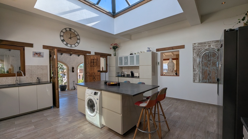 Moderne keuken met kookeiland en een groot glazen dakvenster voor veel lichtinval. Authentieke houten deuren geven toegang tot de aangrenzende overdekte naya.