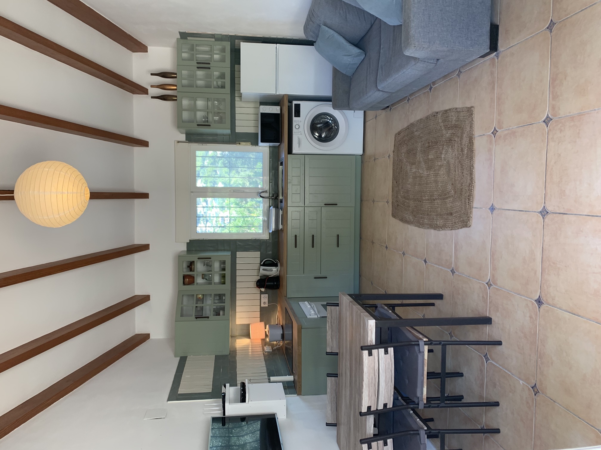 Open woonruimte met een saliegroene keuken, houten balkenplafond en een eethoek op een traditionele tegelvloer met decoratieve hoekaccenten.