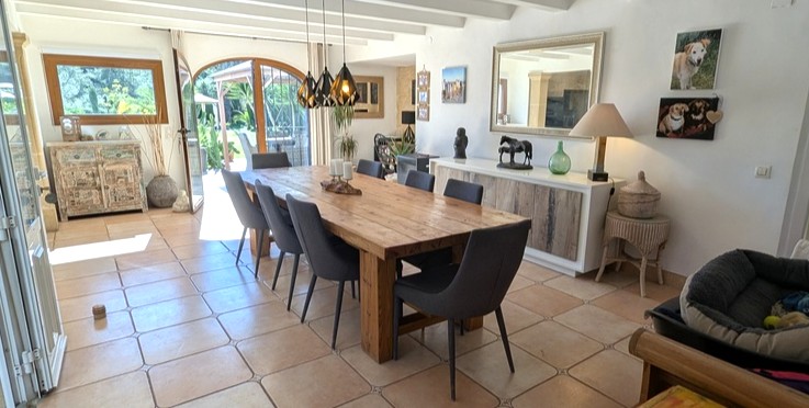 Ruime eethoek met een robuuste houten tafel, wit balkenplafond en terracotta tegels, met directe toegang tot de tuin via een karakteristieke boogdeur.