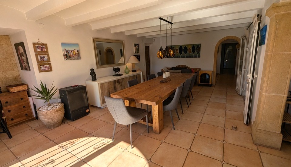 Ruime eetkamer met een grote massief houten tafel, terracotta vloertegels en een wit balkenplafond. Een Tosca-stenen pilaar en boogdeur benadrukken het traditionele karakter van de finca.