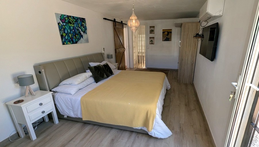 Slaapkamer met houten vloer, een rustieke houten schuifdeur en een hangende lantaarn. Voorzien van airconditioning, wand-tv en een bed met grijs hoofdbord.