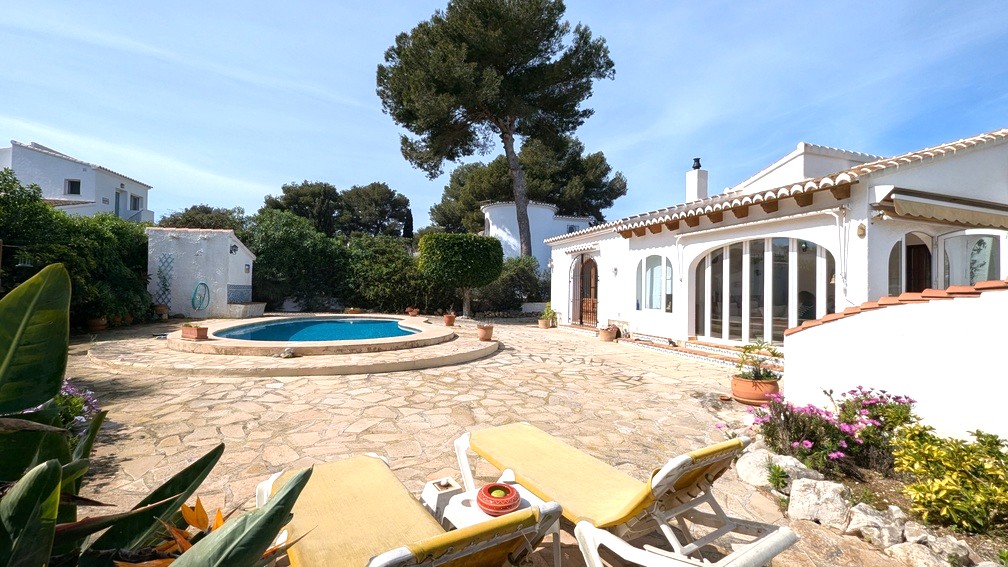 Exterieur van de mediterrane villa met zwembad, natuurstenen terras en witte gevel met houten balken en grote gewelfde glazen deuren.