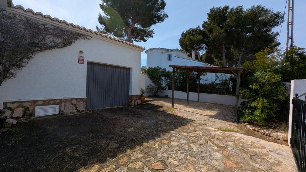 Garage met grijze deur en houten carport, voorzien van een oprit met natuursteen en een witte gevel met stenen plint.