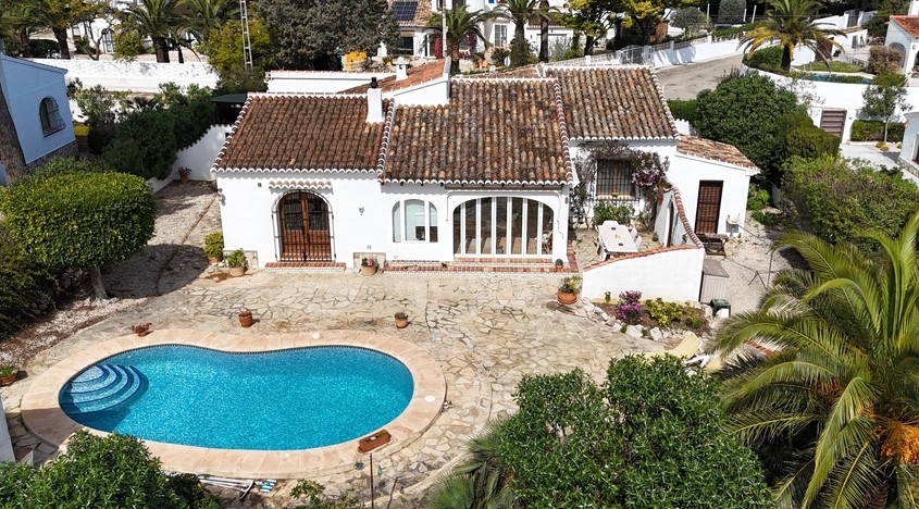 Luchtfoto van de villa met niervormig zwembad, groot natuurstenen terras en mediterrane architectuur met terracotta dakpannen en witte gevels.