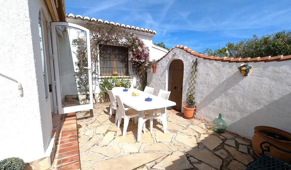 Privé-buitenpatio met natuurstenen bestrating, een witte eethoek en traditionele mediterrane architectuur met boogdeuren en terracotta dakpannen.