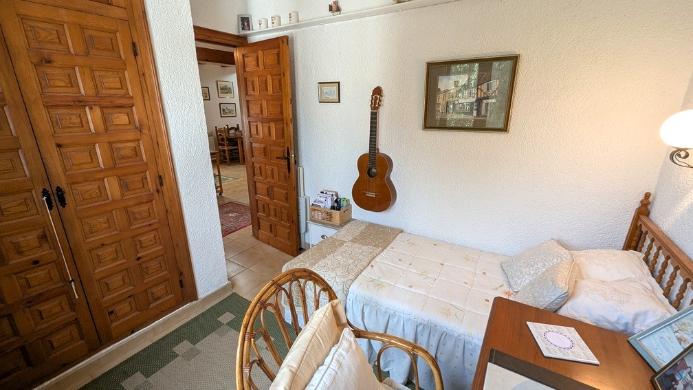Slaapkamer met eenpersoonsbed, houten inbouwkasten met traditionele panelen en witte structuurwanden. Een open deur biedt zicht op de gang en woonruimte.