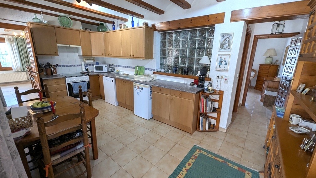 Traditionele keuken met houten plafondbalken, licht houten kasten en een wand van glasbouwstenen voor extra natuurlijke lichtinval.