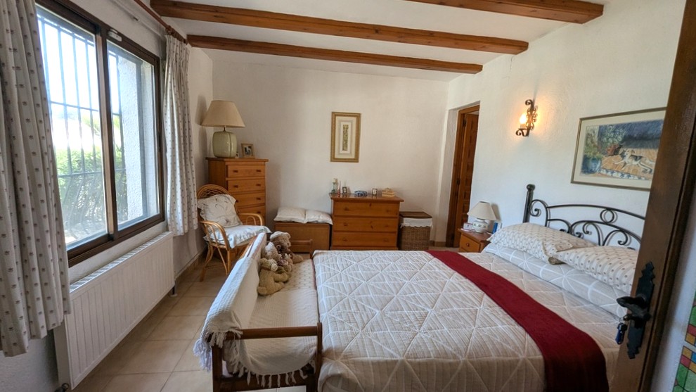 Traditionele slaapkamer met houten plafondbalken, een smeedijzeren bedframe en klassieke houten meubels. De kamer geniet van natuurlijk licht en een radiator.