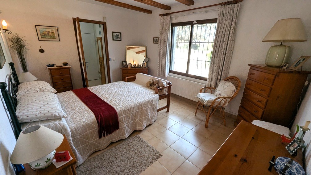 Traditionele slaapkamer met houten plafondbalken, tegelvloer en een radiator onder het raam voor optimaal comfort en natuurlijk lichtinval.