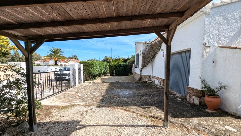 Zicht vanuit de houten carport op de bestrate oprit, de garage en het smeedijzeren toegangshek van de woning.