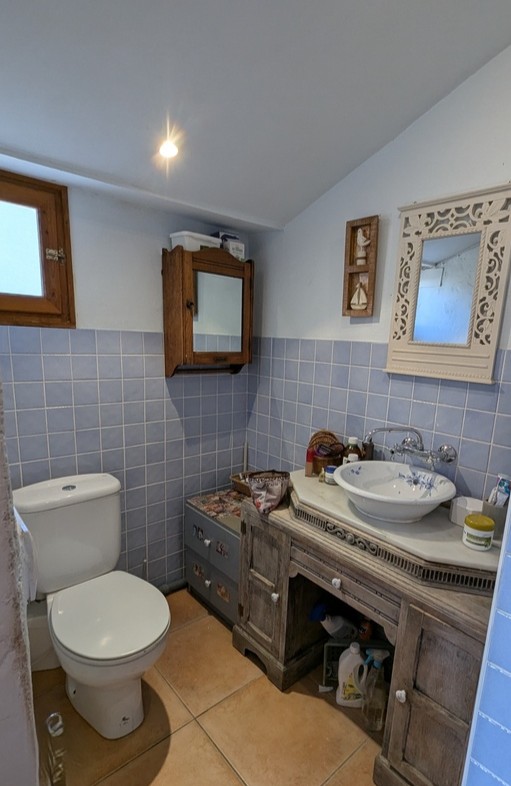 Badkamer met een rustiek houten wastafelmeubel, marmeren blad, bloemige keramische waskom en lichtblauwe wandtegels gecombineerd met een terracotta vloer.