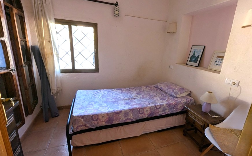 Gezellige slaapkamer met een eenpersoonsbed, terracotta tegelvloer en een decoratieve nis in de muur. Een raam met traditionele tralies zorgt voor natuurlijk licht.