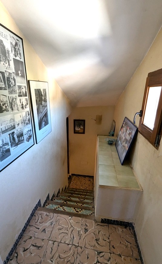 Interne trap met traditionele patroontegels en decoratieve mozaïekstootborden. Een houten raam en ingelijste kunstwerken sieren de lichte trapopgang.