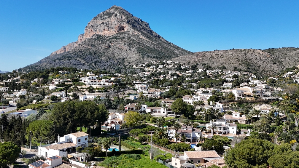Panoramisch uitzicht op de Montgó-berg over het woonlandschap van Javea, met traditionele witte villa's en weelderig mediterraan groen onder een heldere hemel.