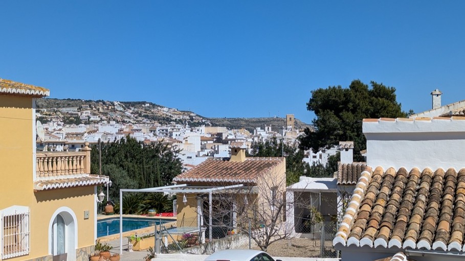 Panoramisch uitzicht vanaf het boventerras op Javea Pueblo, met traditionele pannendaken, het privézwembad en de omliggende heuvels onder een blauwe hemel.