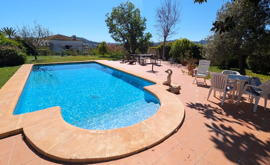 Privézwembad met blauwe mozaïektegels, omgeven door een ruim terras van terracotta en een volgroeide mediterrane tuin met vrij uitzicht op de bergen.