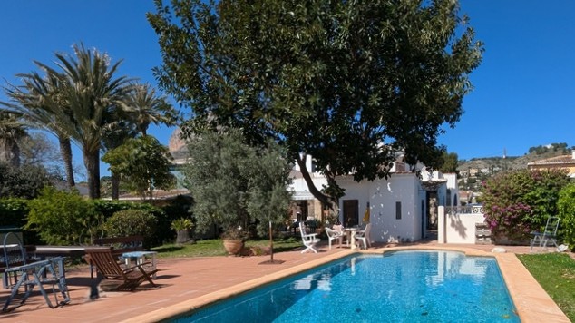 Privézwembad met terracotta terras, omgeven door een volgroeide mediterrane tuin met palmbomen en uitzicht op de iconische Montgó-berg.