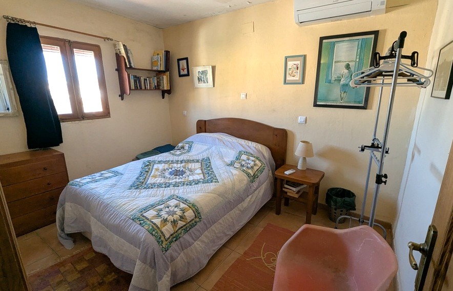 Slaapkamer met houten meubilair, tegelvloer en airconditioning. Voorzien van wandplanken, een klassieke ladekast en natuurlijk licht via een houten raamkozijn.