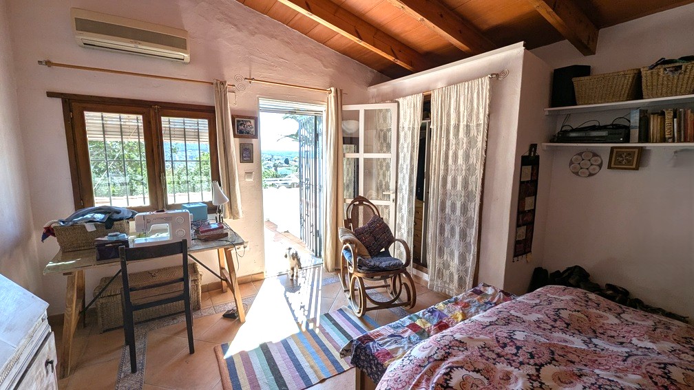 Slaapkamer met houten plafondbalken, terracotta vloer en directe toegang tot een terras met uitzicht op het landschap. Voorzien van airconditioning en een werkplek.
