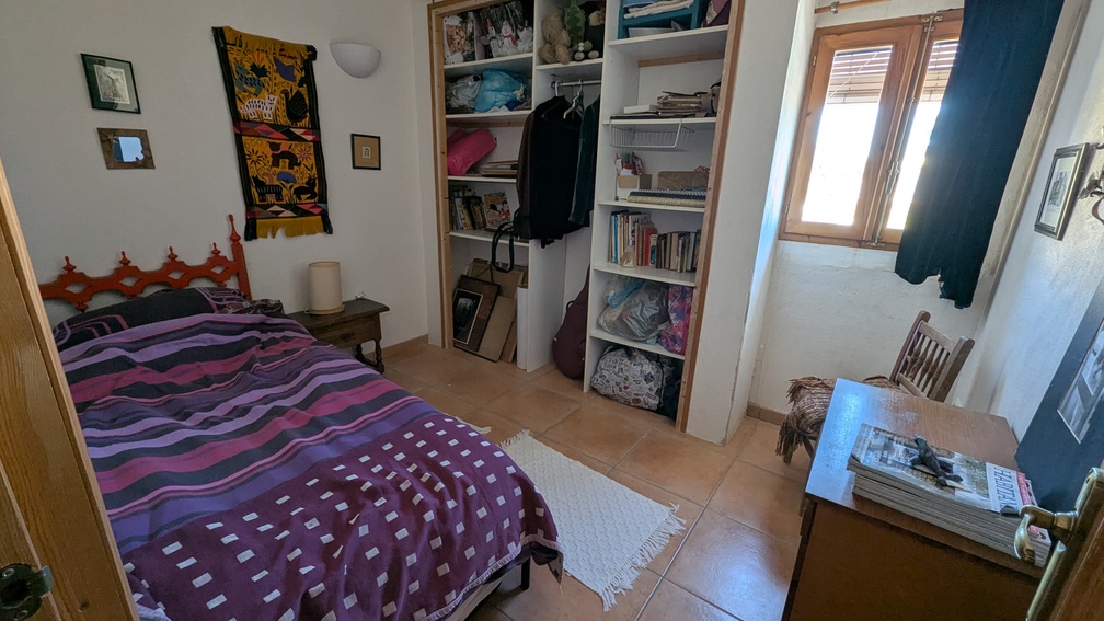 Slaapkamer met terracotta vloertegels, ingebouwde open kasten en een houten raamkozijn. De ruimte beschikt over een eenpersoonsbed en een houten bureau met natuurlijk licht.
