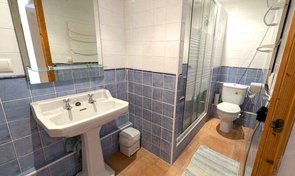Traditionele badkamer met blauw-witte wandtegels, een klassieke wastafel op zuil, terracotta vloer en een inloopdouche met glazen wand.