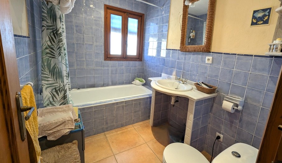 Traditionele badkamer met blauwe wandtegels, een ingebouwd bad en een marmeren wastafelblad. Voorzien van terracotta vloertegels en een houten raamkozijn.