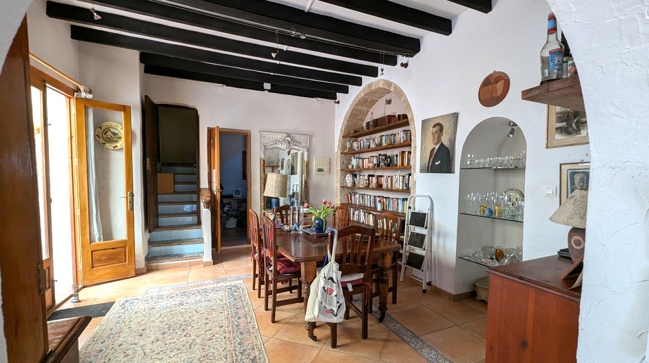 Traditionele eetkamer met donkere houten plafondbalken, een ingebouwde boekenkast in een Tosca stenen boog en terracotta vloeren bij de betegelde trap.