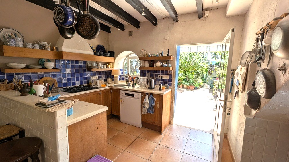 Traditionele keuken met donkere houten plafondbalken, blauwe tegelwand en houten kasten, met directe toegang tot het zonnige tuinterras.