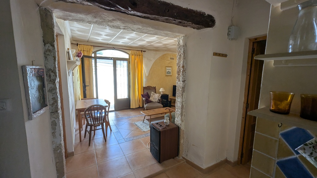 Traditionele Tosca stenen boog met houten balk die leidt naar een lichte woonkamer met terracotta vloeren en een halfronde glazen deur.