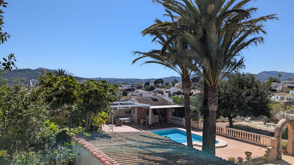 Verhoogd uitzicht op het privézwembad en terras, voorzien van een traditionele buitenkeuken, palmbomen en weids uitzicht over de omgeving van Javea.