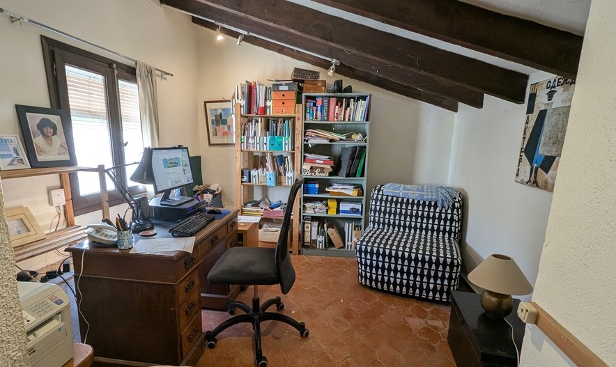 Werkkamer met traditionele terracotta vloertegels, donkere houten plafondbalken en een klassiek houten bureau bij het raam voor natuurlijk licht.