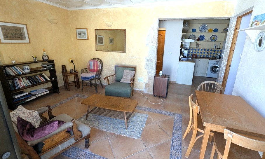 Woonkamer van het gastenverblijf met terracotta vloertegels, decoratieve randen en een boog van Tosca-natuursteen die toegang biedt tot de compacte keuken.