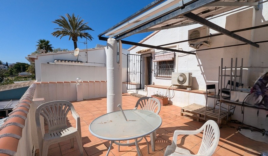 Zuidgericht terras op de eerste verdieping met terracotta tegels, een metalen pergolastructuur en airconditioningunits, met uitzicht op de nabijgelegen palmbomen.