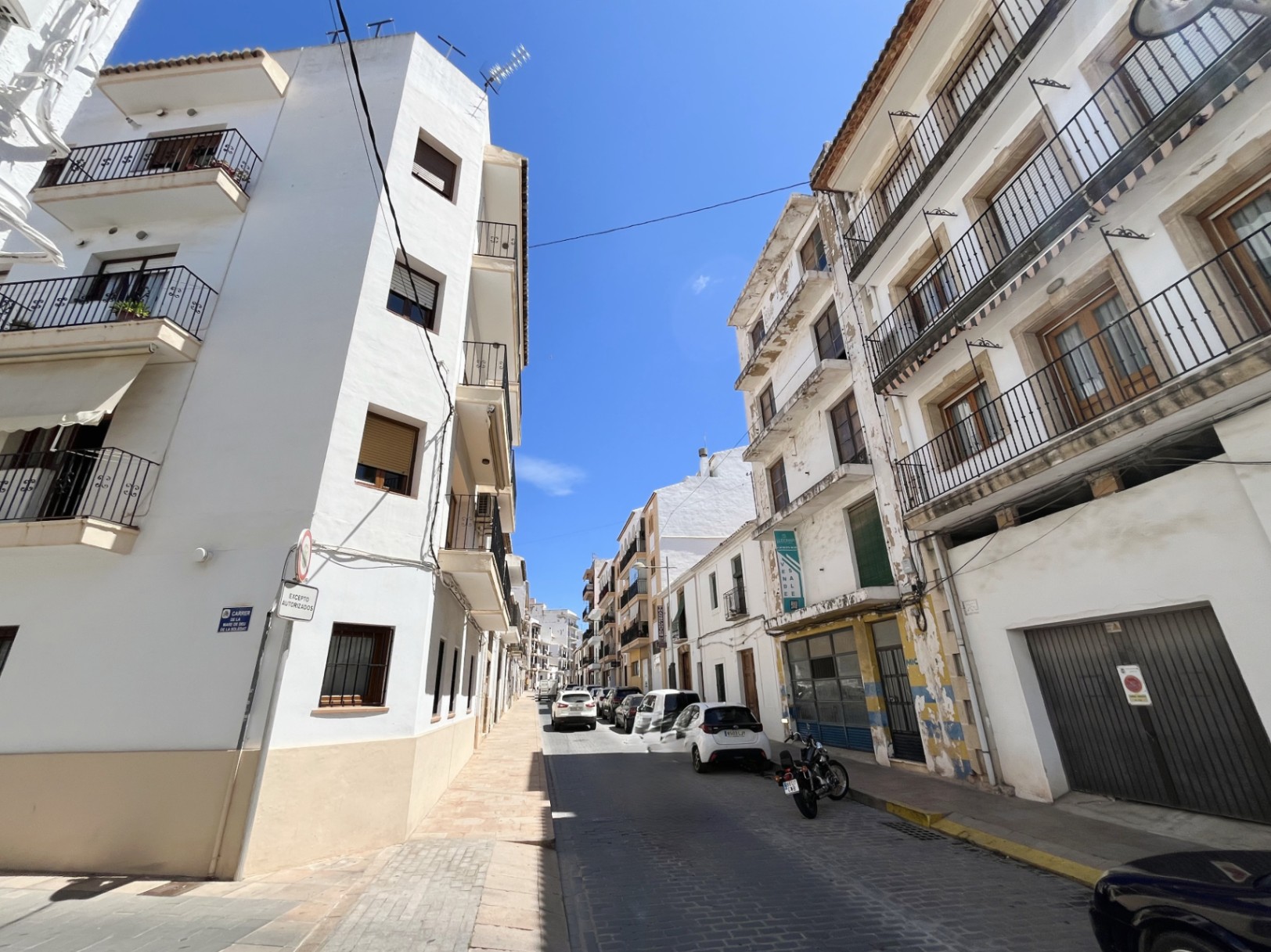 Buitenaanzicht van het gebouw met vier verdiepingen in het centrum van Jávea, met een witte gevel, smeedijzeren balkons en een ruime commerciële ruimte op de begane grond.