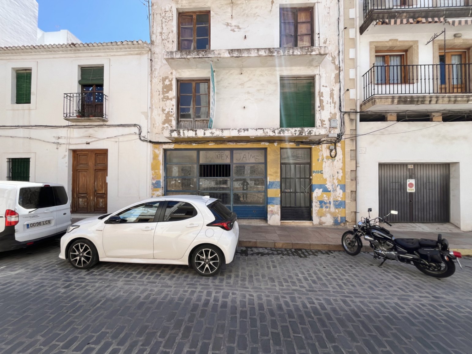 Buitengevel van het gebouw in Jávea met een commerciële ruimte op de begane grond, balkons op de verdiepingen en houten kozijnen aan een traditionele kasseienstraat.