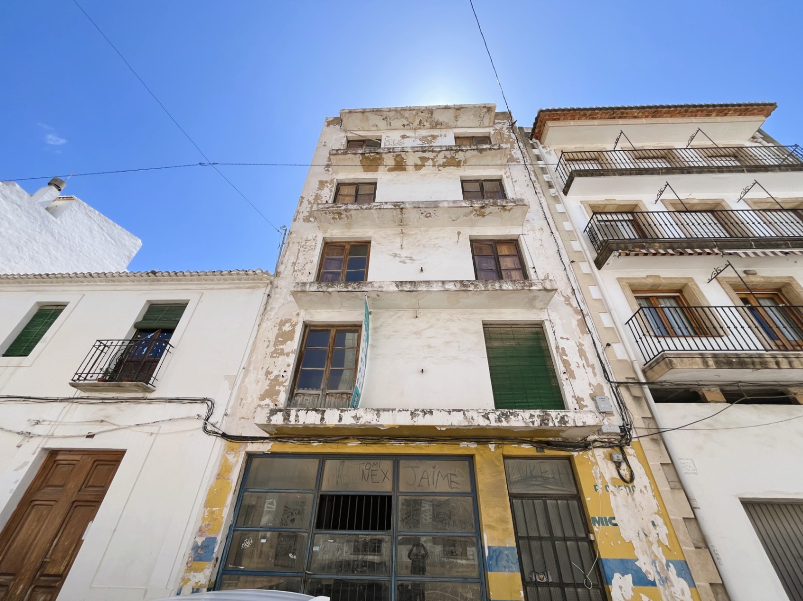 Gevel van vier verdiepingen met een commerciële ruimte op de begane grond. Het pand beschikt over houten kozijnen en balkons, perfect voor een volledige renovatie in Jávea.
