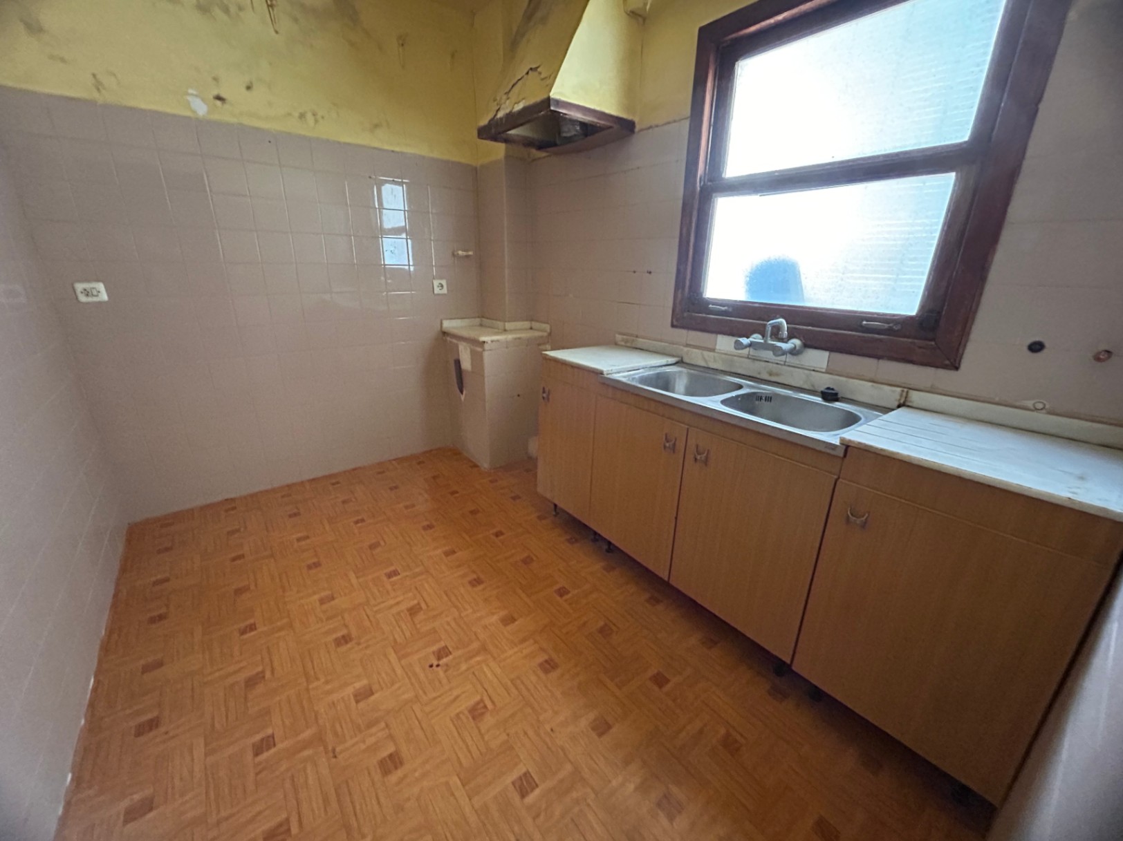 Originele keuken met dubbele roestvrijstalen spoelbak, houten kasten en patroontegels. Een houten raam zorgt voor natuurlijk licht in dit renovatieproject.