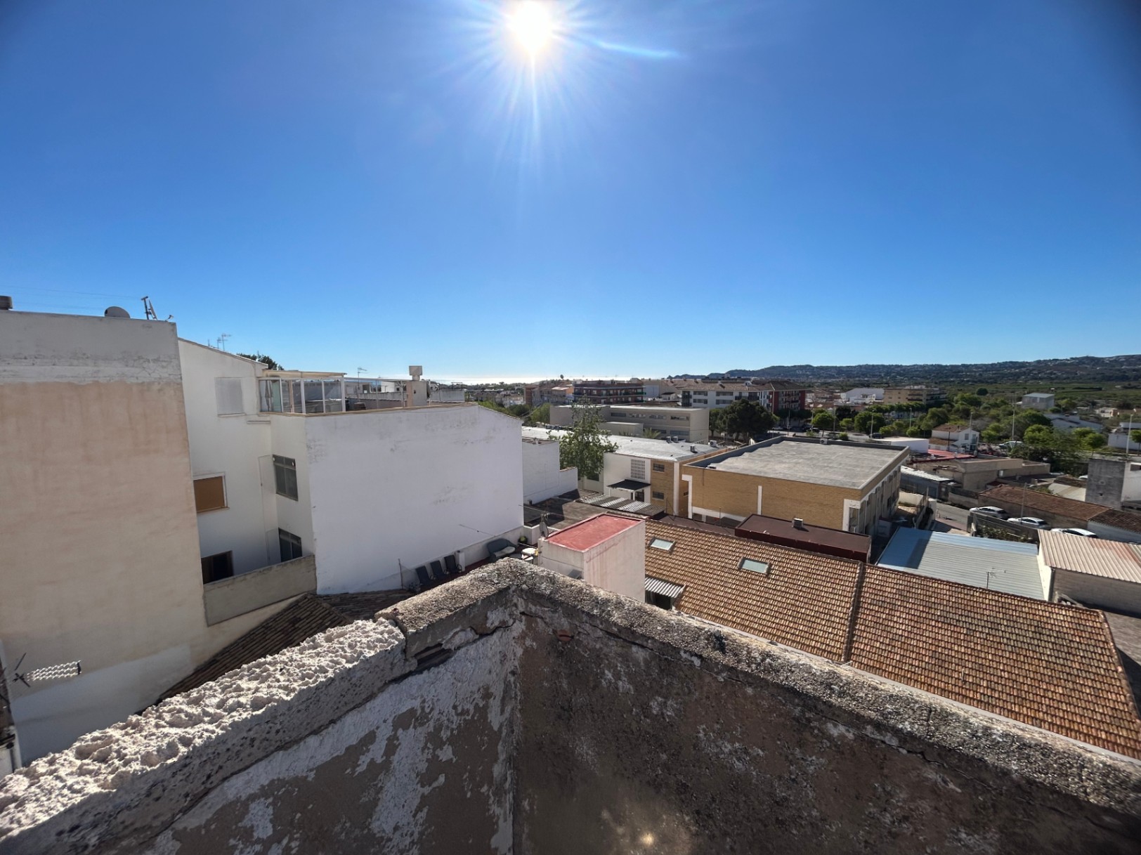 Panoramisch uitzicht vanaf het dakterras over het centrum van Jávea en de Middellandse Zee, met traditionele pannendaken en verre bergsilhouetten in de zon.