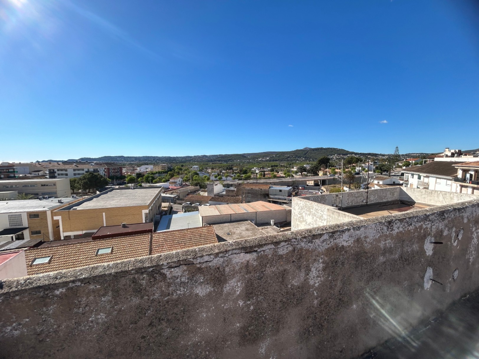Panoramisch uitzicht vanaf het gemeenschappelijke dakterras over de stad Jávea en de omliggende groene heuvels onder een heldere, zonnige hemel.