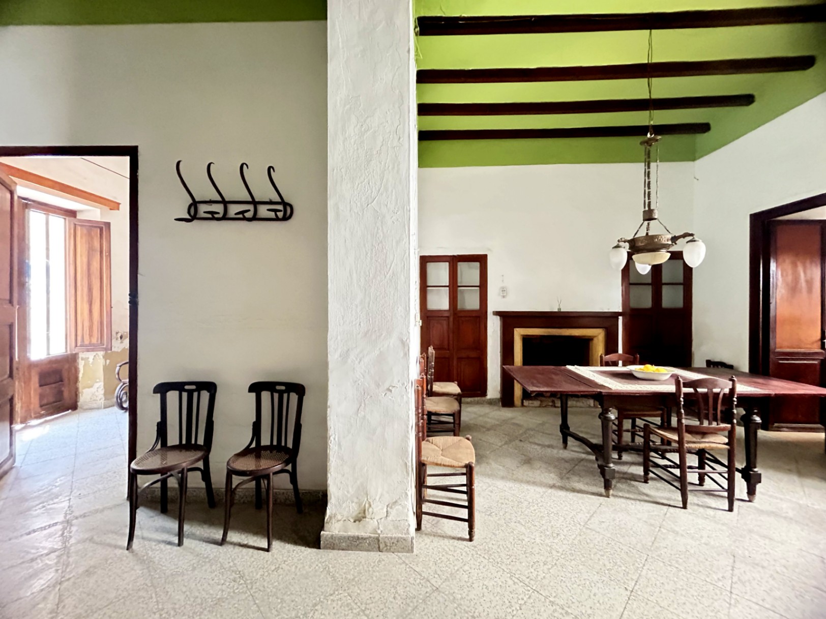 Traditionele eetkamer met originele houten balken, hoge groene plafonds en een klassieke open haard. Antiek meubilair en natuurlijk licht benadrukken de sfeer.