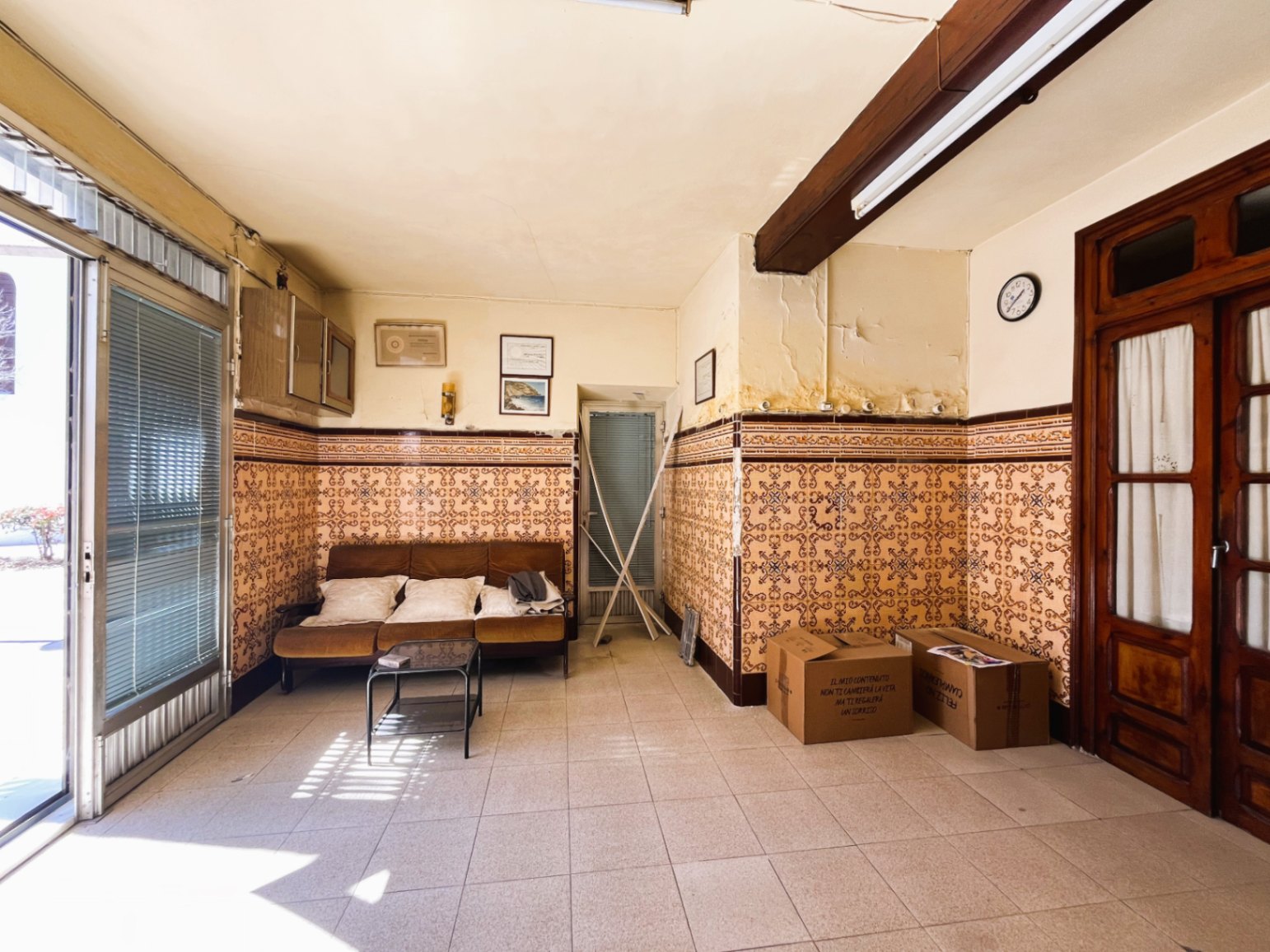Entree-woonkamer met traditionele wandtegels, een zichtbare houten balk en een grote glazen deur die zorgt voor overvloedig natuurlijk licht.
