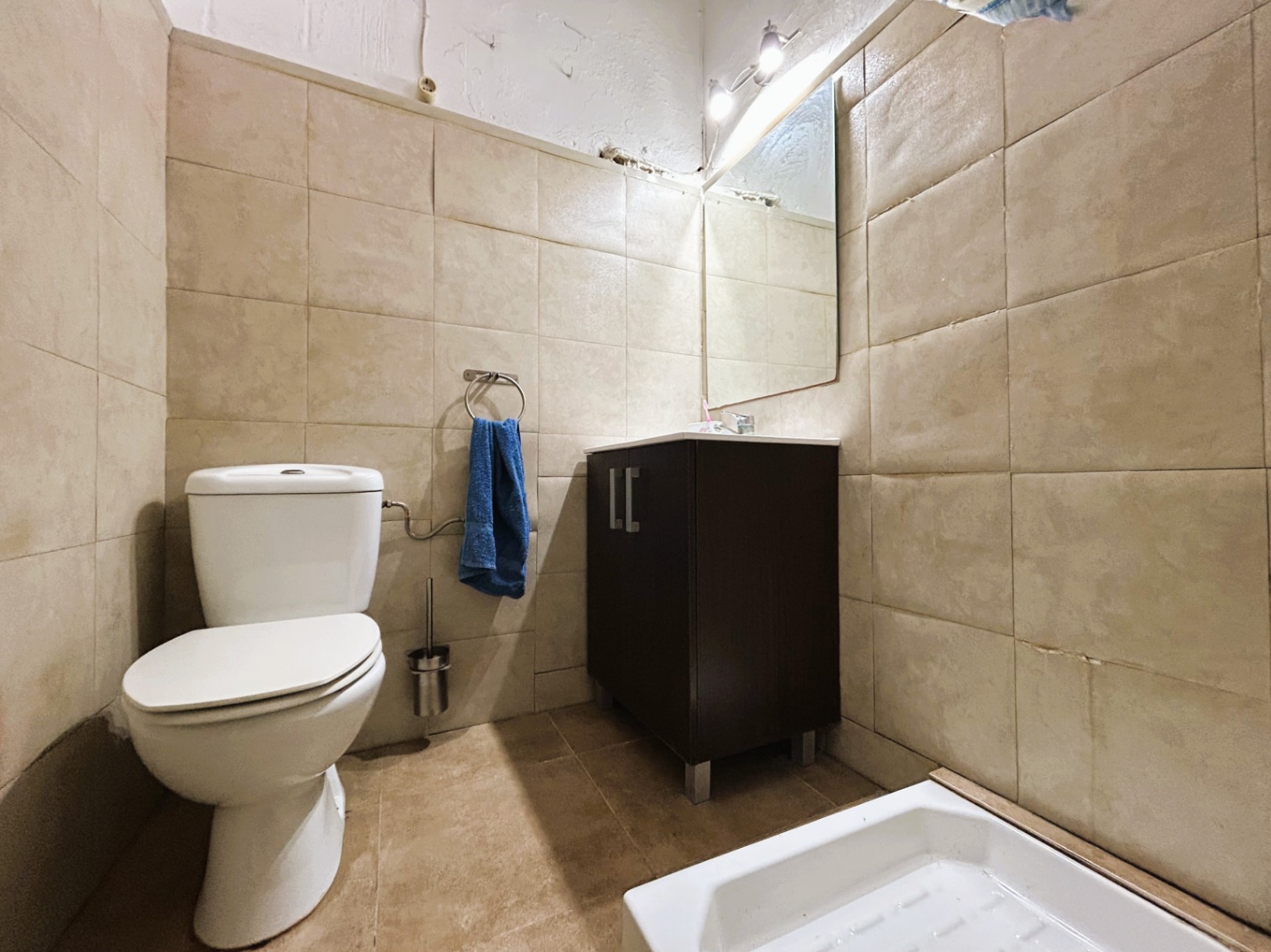Functionele badkamer met beige wandtegels, een wit keramisch toilet en een donkerhouten wastafelmeubel met verlichte spiegel.