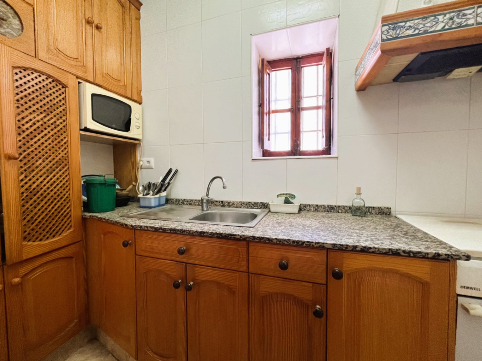 Gesloten keuken met traditionele houten kasten, een granieten werkblad met dubbele spoelbak en een authentiek houten raam met luiken.