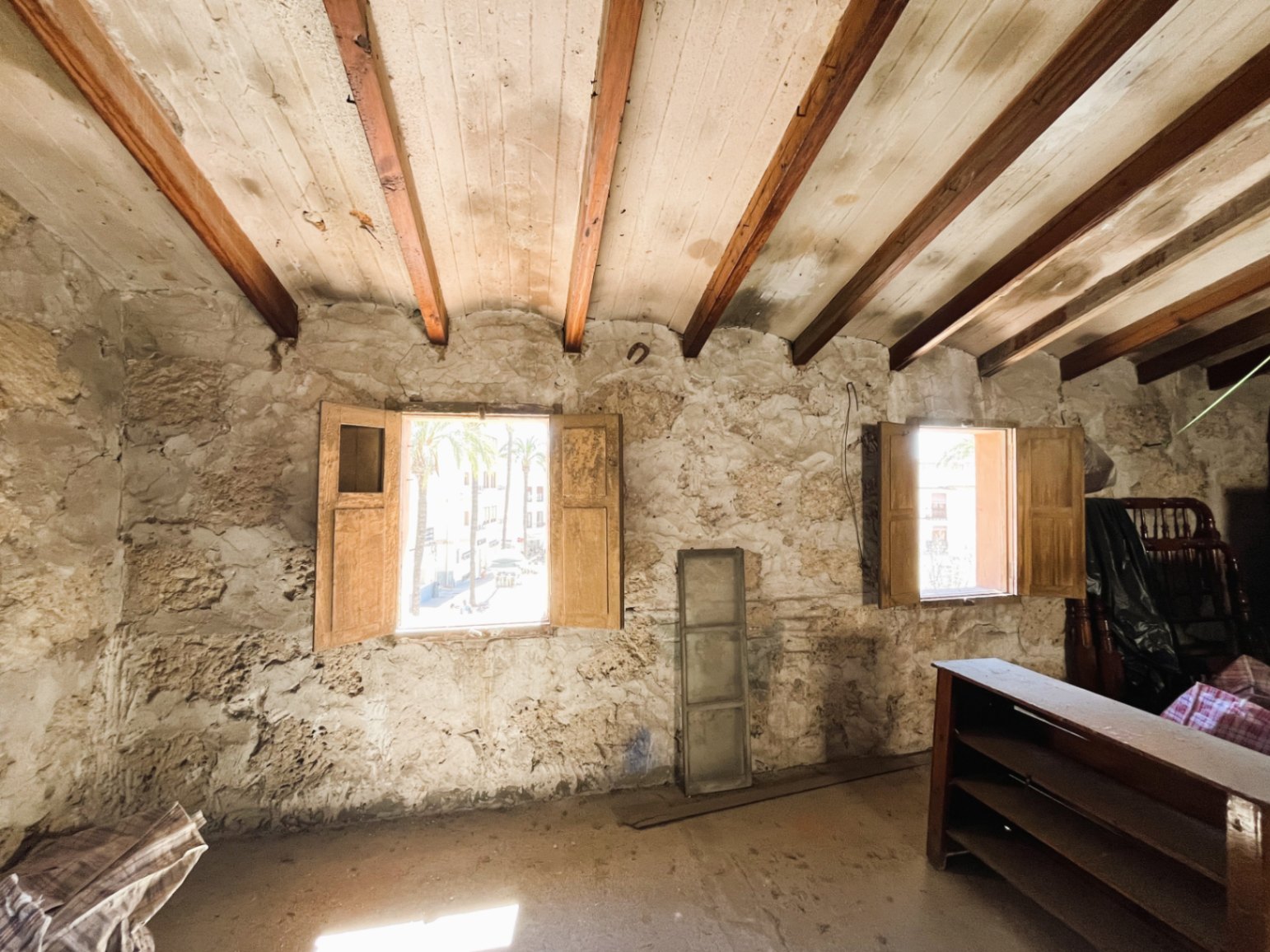 Kamer met originele natuurstenen muren en houten balkenplafond. Twee ramen met houten luiken bieden natuurlijk licht en uitzicht op de historische oude stad.