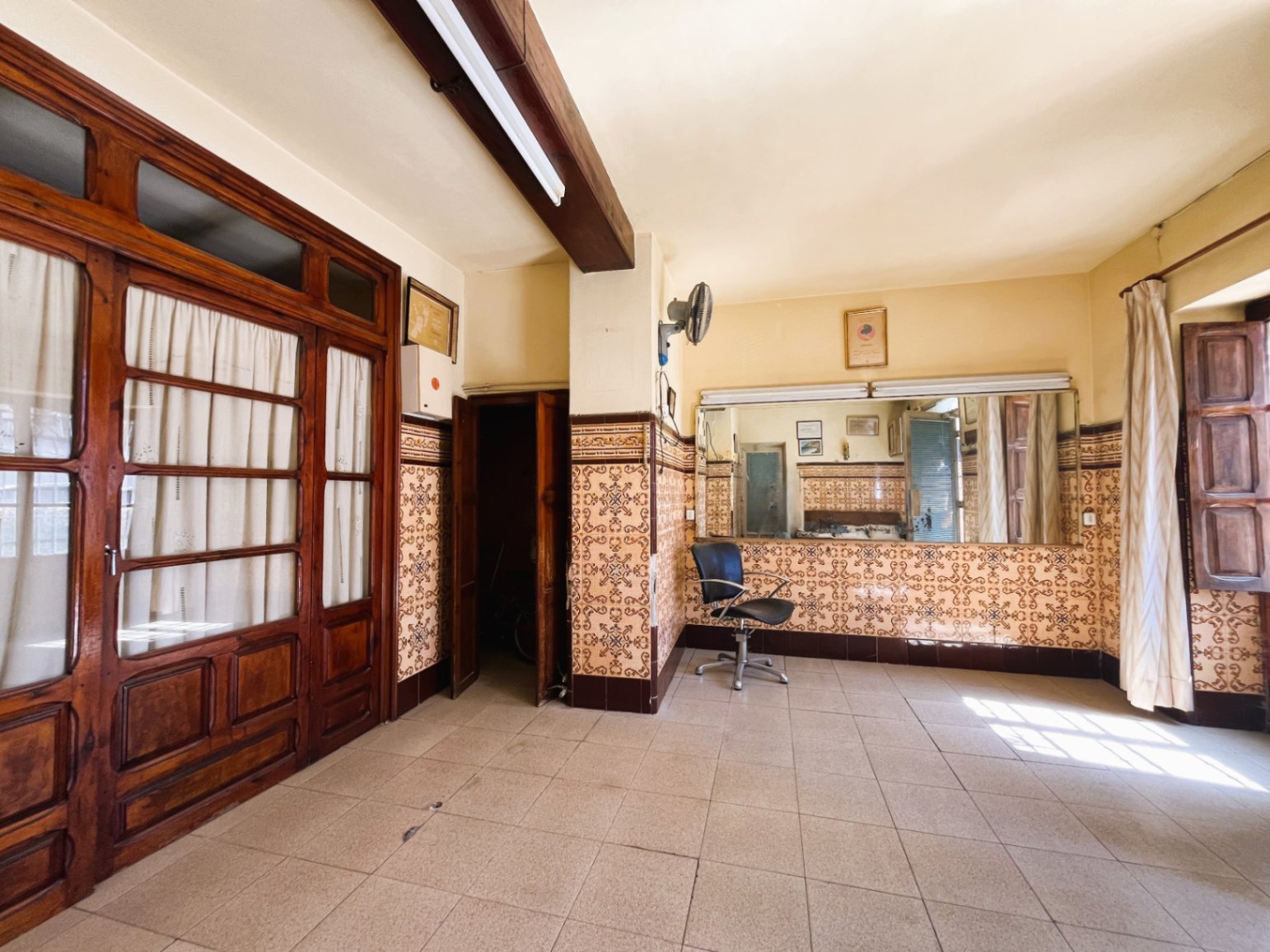Ruime kamer met traditionele wandtegels, houten plafondbalken en grote glazen deuren die de authentieke Spaanse stijl van het pand behouden.