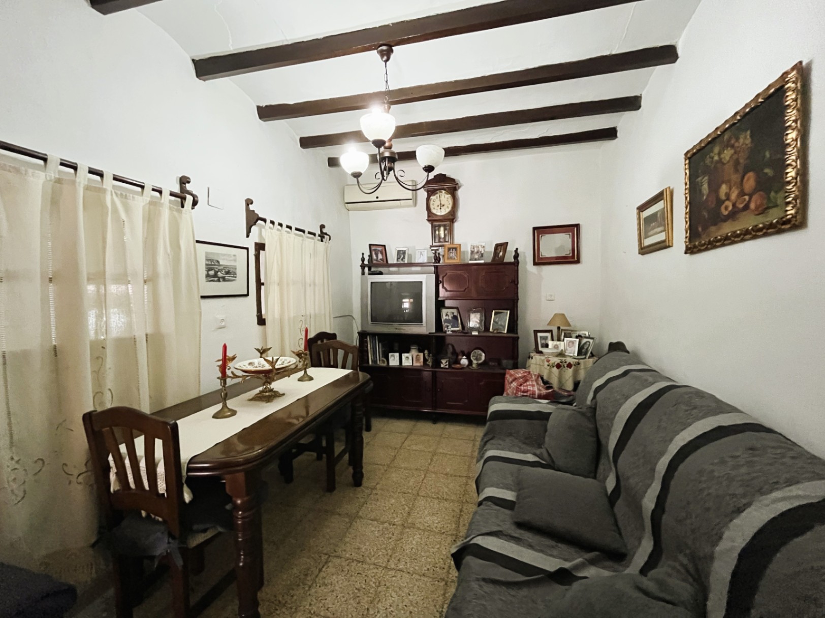 Traditionele woon-eetkamer met donkere houten plafondbalken, terrazzovloer en klassieke donkerhouten meubels in het historische centrum van Jávea.