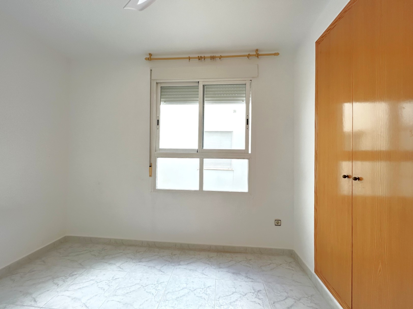 Lichte slaapkamer met vloertegels in marmerlook, een ingebouwde houten kledingkast en een wit aluminium raam met rolluik.