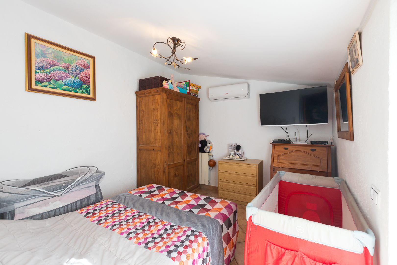 Lichte slaapkamer met schuin plafond, airconditioning en klassieke houten meubels, momenteel ingericht met praktische kinderbedden.