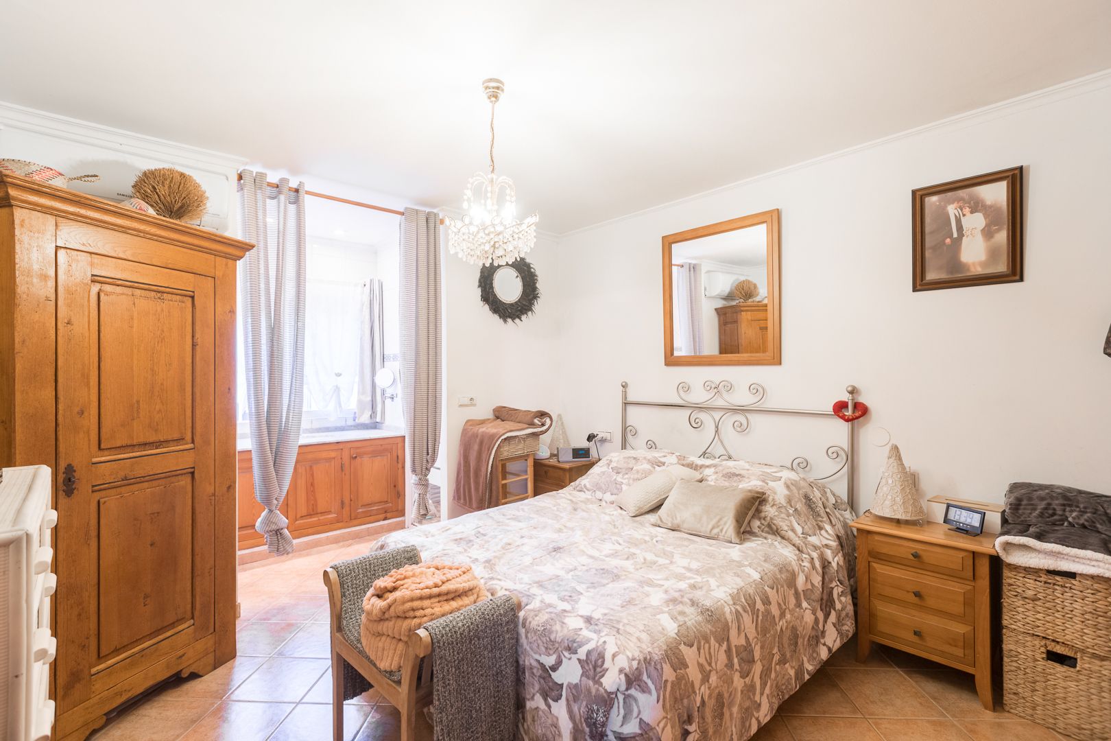 Slaapkamer met keramische tegels, klassieke houten kast en smeedijzeren hoofdbord. Voorzien van airconditioning, een kristallen kroonluchter en natuurlijk licht.